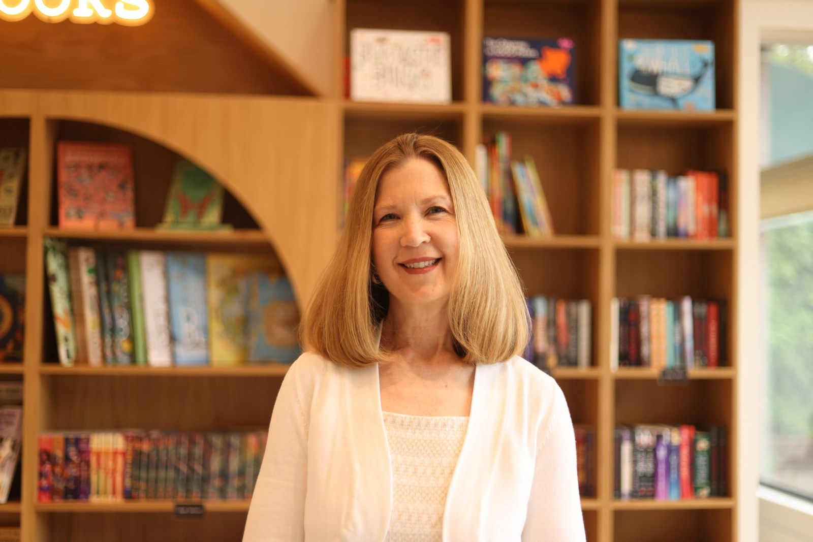 A smiling bookshop owner standing in front of her shelves
